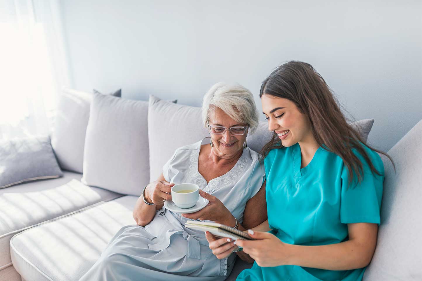 Senior woman and caregiver on couch with coffee
